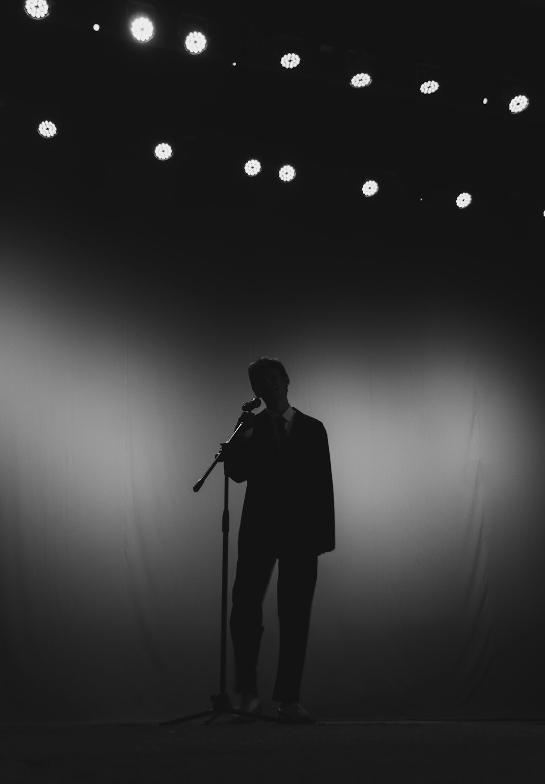 Calm television presenter speaking into a microphone under studio lights